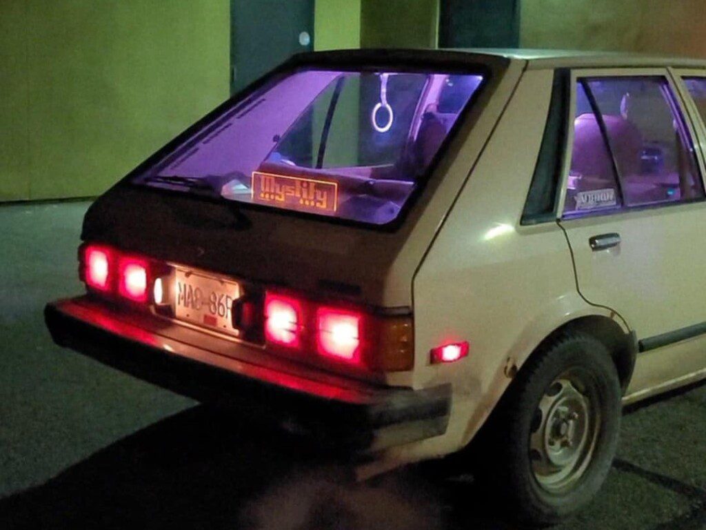 Retro car with purple interior lighting and vintage decal parked at night.