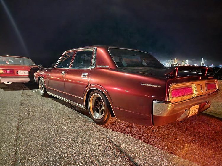 Classic maroon sedan parked at night with city lights in the background, showcasing vintage style and design.