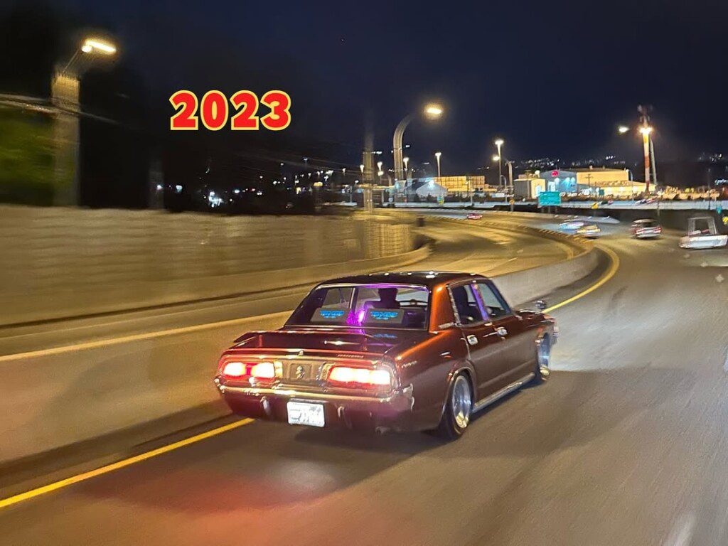 Vintage car driving on city highway at night, with glowing 2023 text in the background.