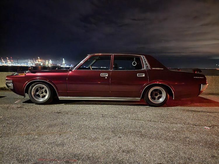 Vintage red sedan parked at night by waterfront, city lights in background. Classic car enthusiasts delight.