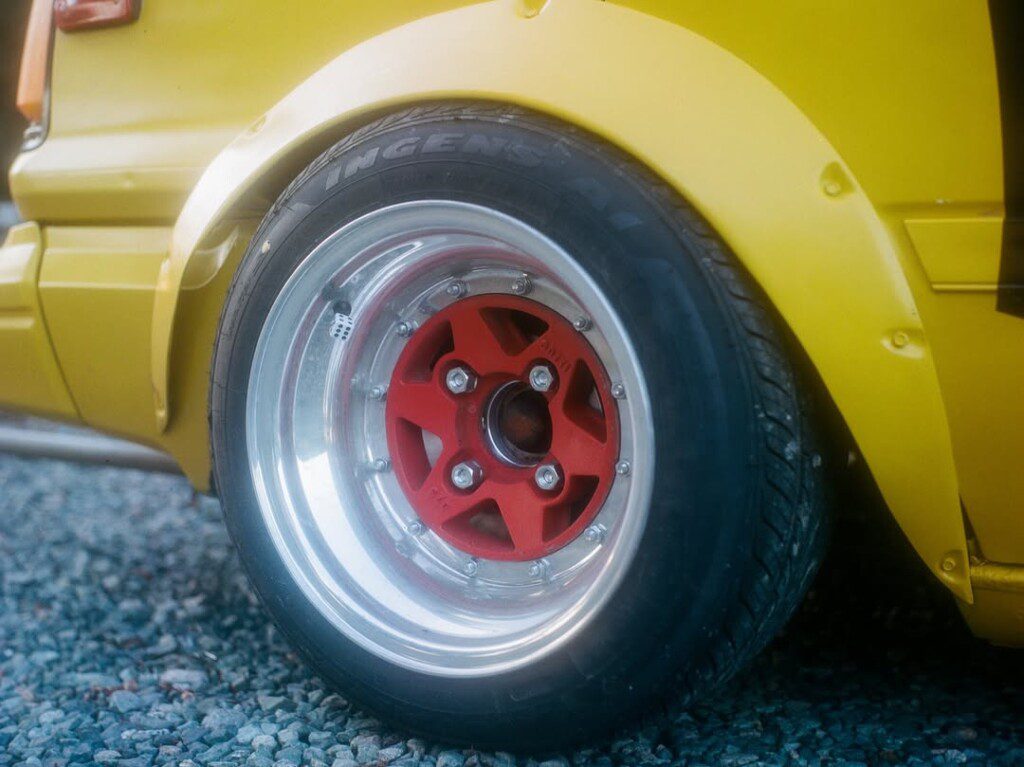 Yellow car with red and chrome wheel on gravel, showcasing stylish automotive design close-up.