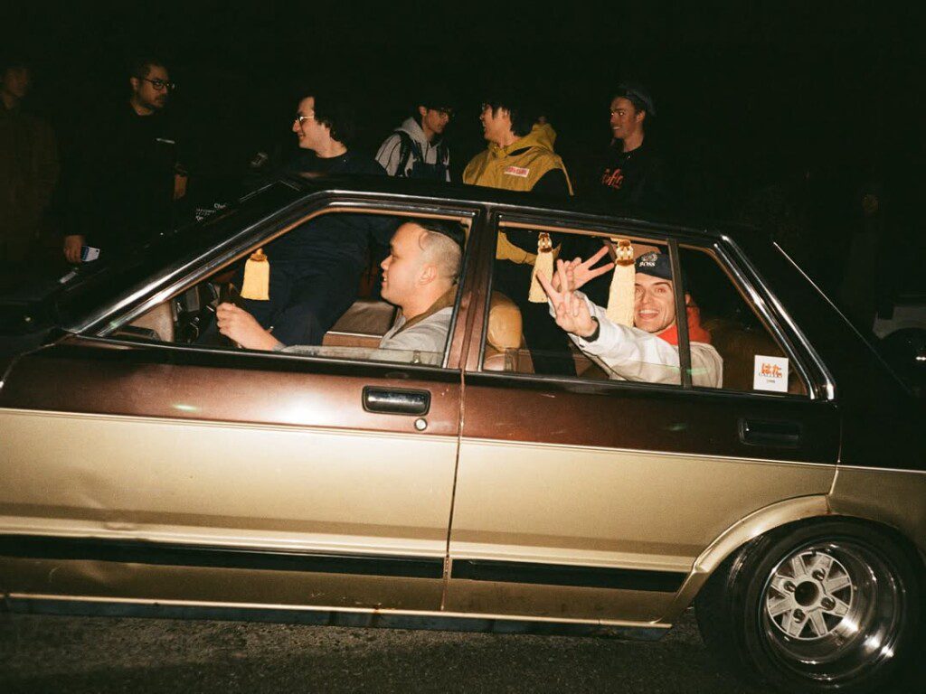 Group of friends in a vintage car at night, smiling and flashing peace signs.