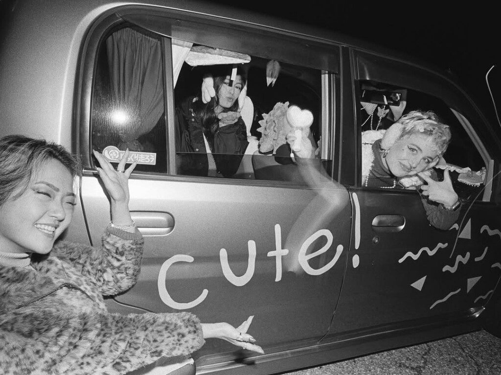 People enjoying a joyful moment around a car with the word cute written on it at night.