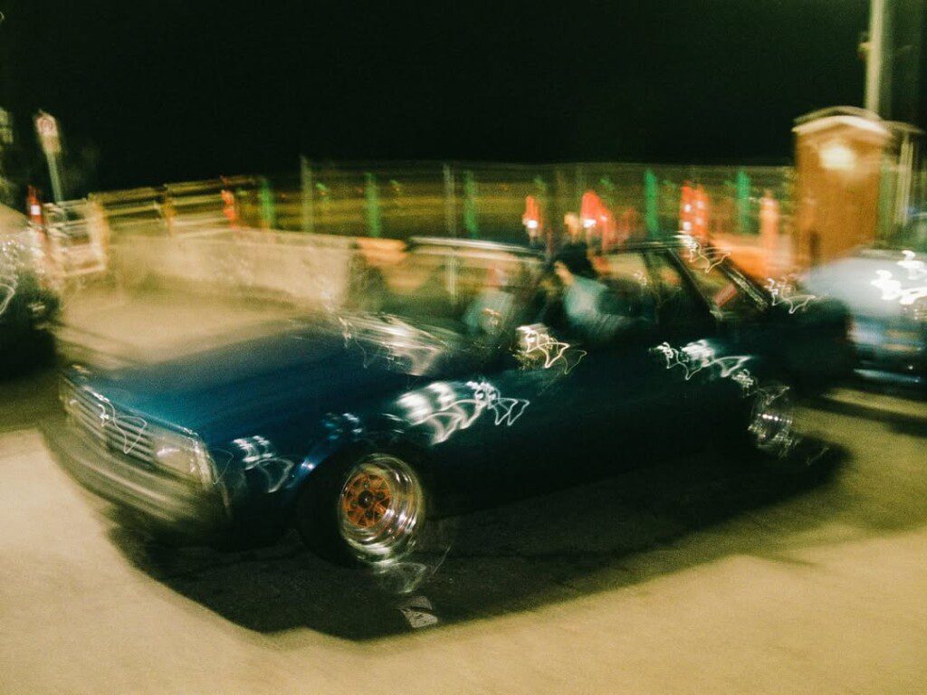 Blurry image of a car driving through a lit street at night, creating a sense of motion and urban dynamism.