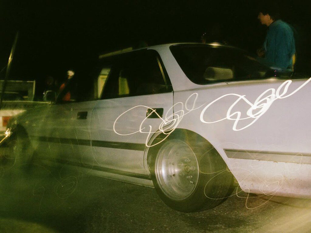Vintage white car with light trails at night, showcasing speed and dynamic movement on the street.