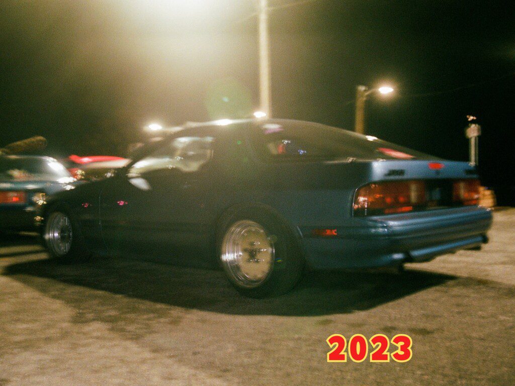 Blurred night street scene with blue car and 2023 text overlay, showcasing a retro automotive vibe.
