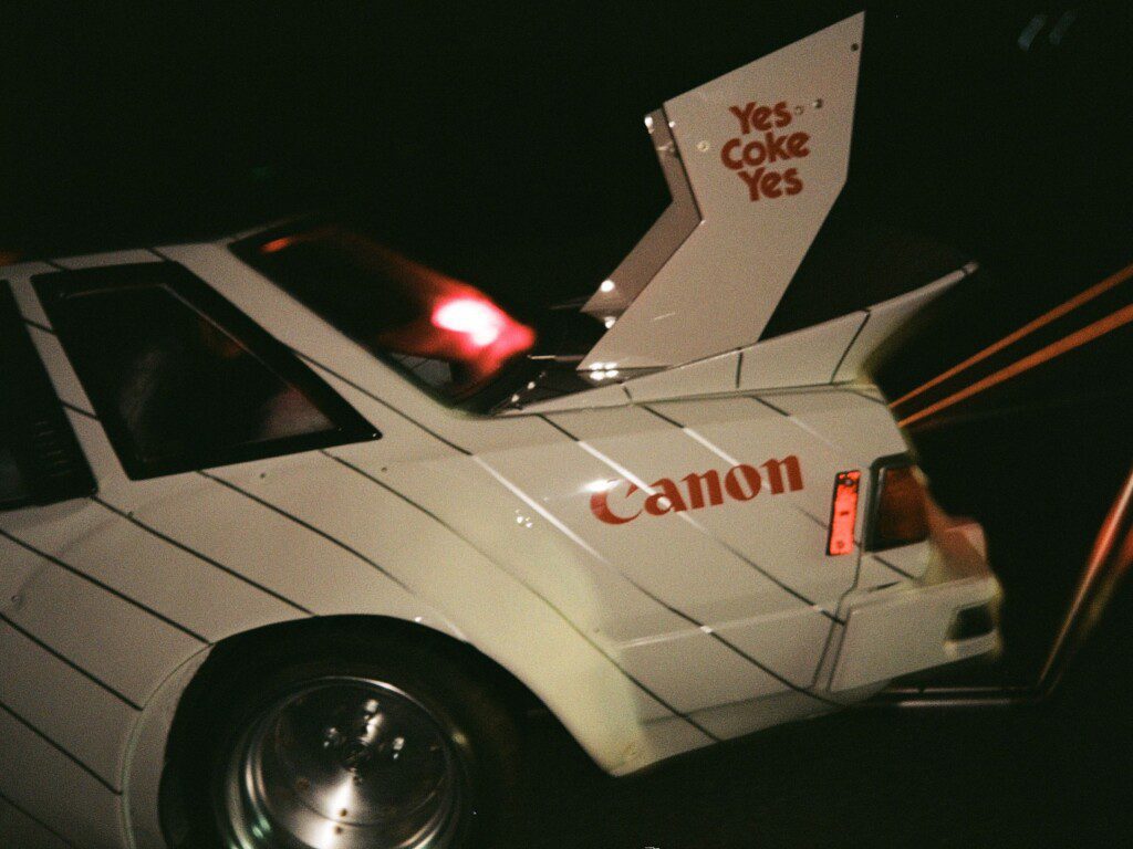 Rear view of a vintage race car with Canon and Coca-Cola branding, featuring a prominent spoiler.