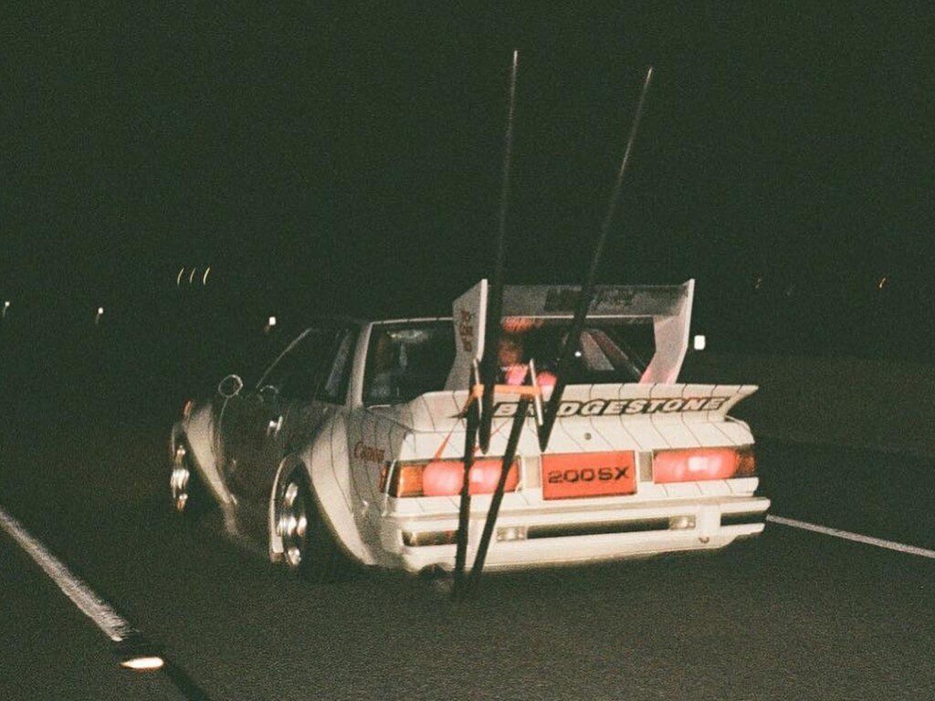 Vintage sports car driving on a highway at night with custom decals and spoiler.