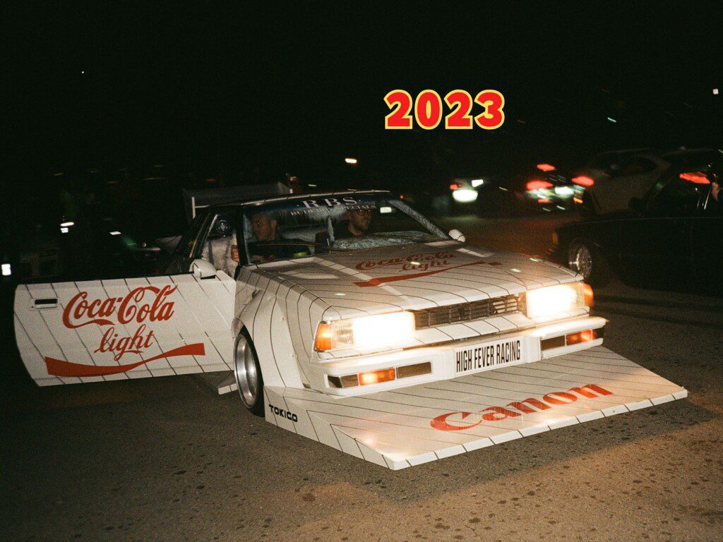 Custom car with Coca-Cola and Canon racing decals at night event, 2023.