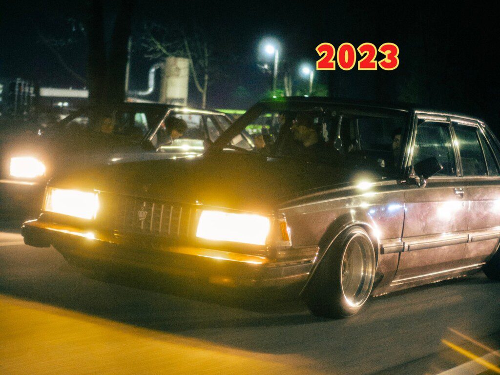 Classic car driving at night with bright headlights, year 2023 overlayed. Vintage style automotive scene.