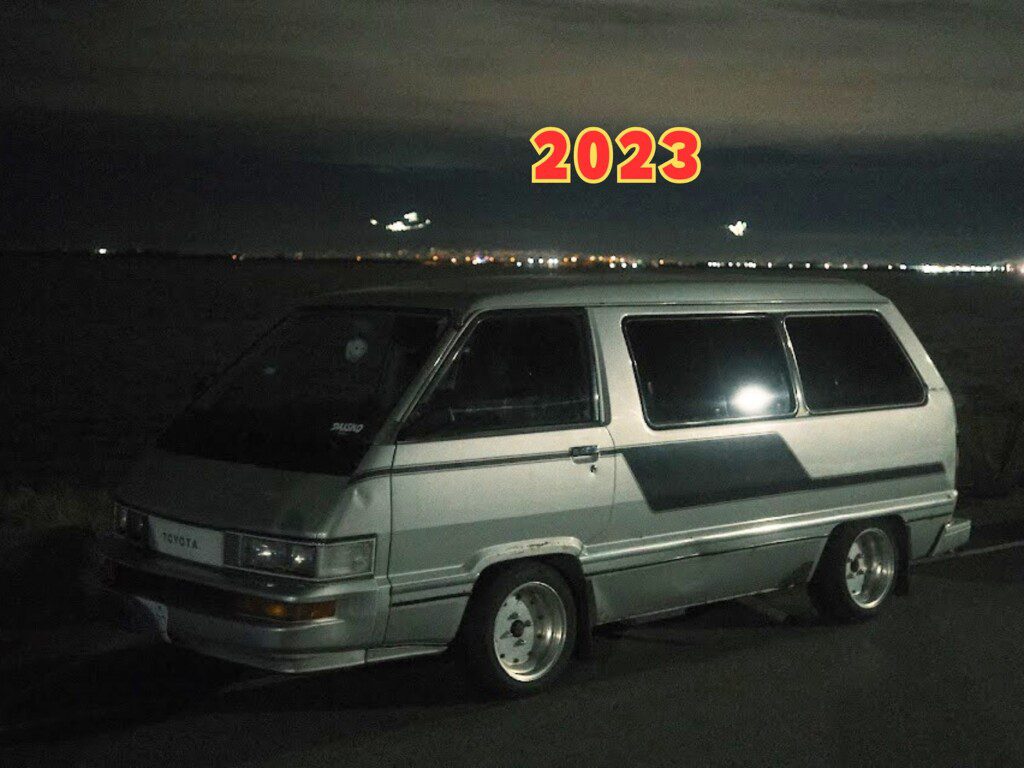 Vintage Toyota van at night with city lights in the background, featuring bold 2023 text above.