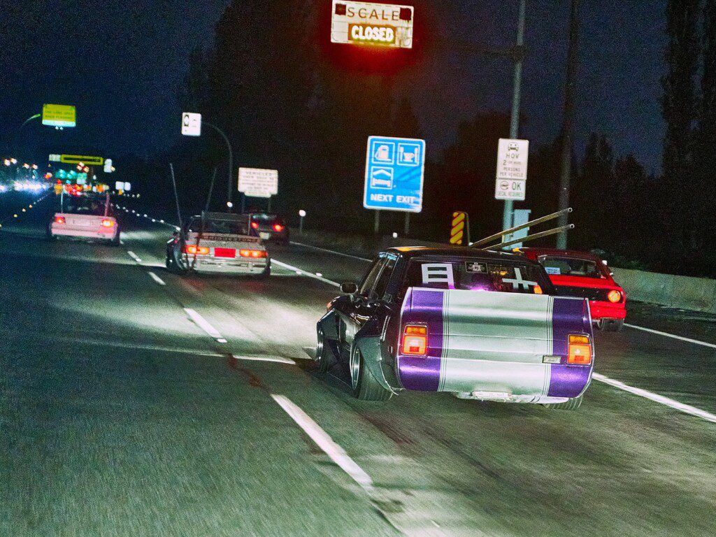 Three vintage cars cruising at night on a highway with neon lights and signs, showcasing a retro street racing vibe.