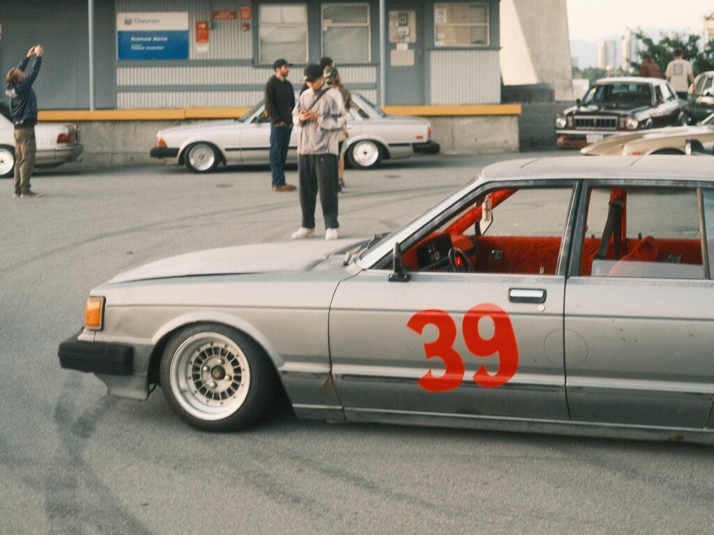 Vintage race car with number 39 at automotive event, people photographing and chatting in the background.