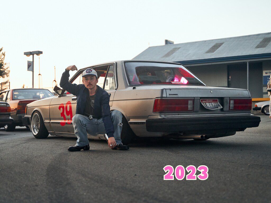 Person posing confidently in front of a retro car with 39 on the side in an urban setting, 2023.
