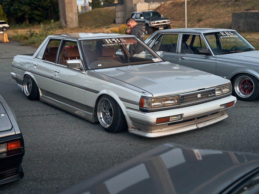 Modified classic car with lowered suspension at a car meet, showcasing custom wheels and vintage styling.