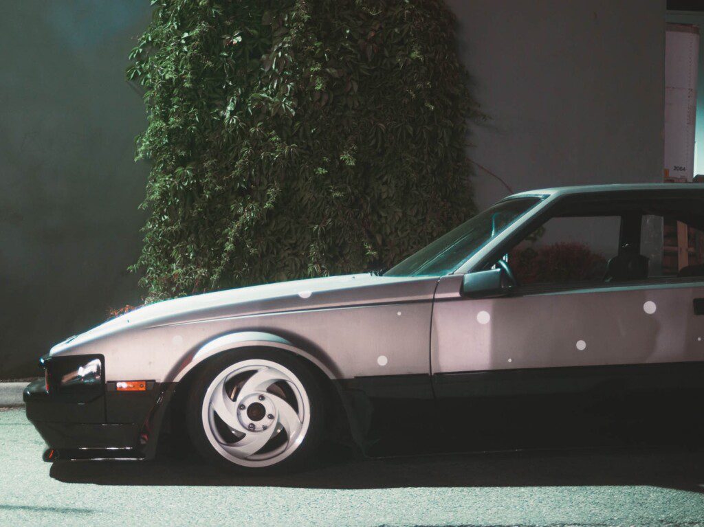 Vintage car with custom wheels parked at night, featuring a sleek design and polka dot pattern on the body.