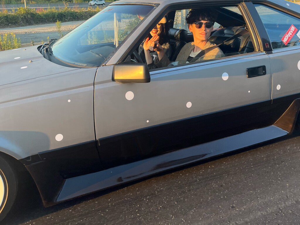 Sports car on highway with two passengers wearing sunglasses, cruising in the sunset.