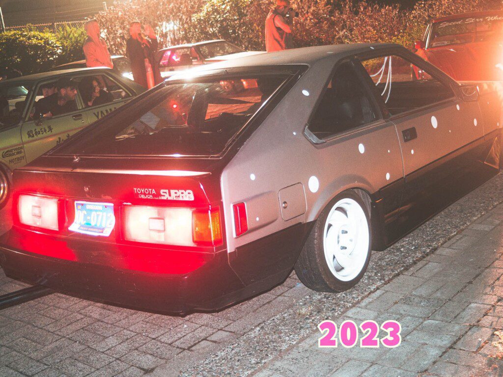 Vintage Toyota Supra in a nighttime car meet, showcasing custom polka dot design and classic styling.
