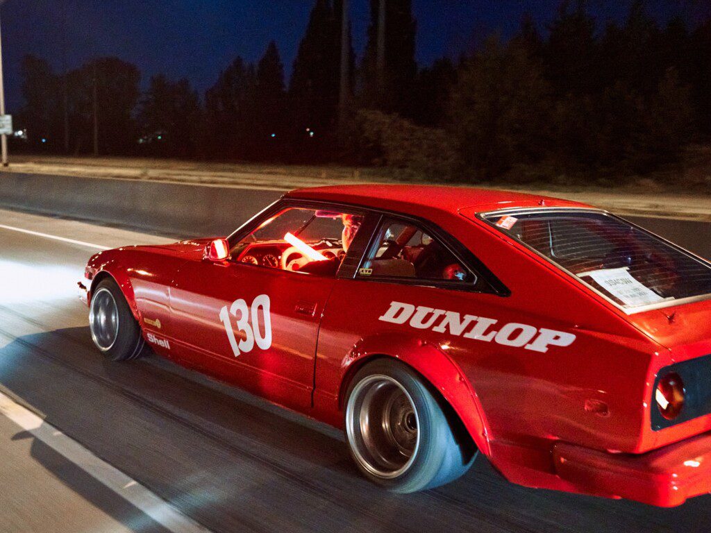 Red sports car with number 130 racing on highway at night, featuring Dunlop branding on the side.