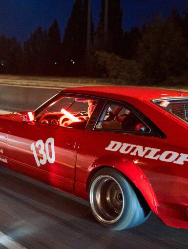 Red sports car with number 130 racing on highway at night, featuring Dunlop branding on the side.