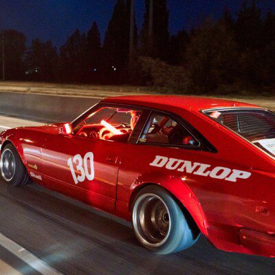 Red sports car with number 130 racing on highway at night, featuring Dunlop branding on the side.