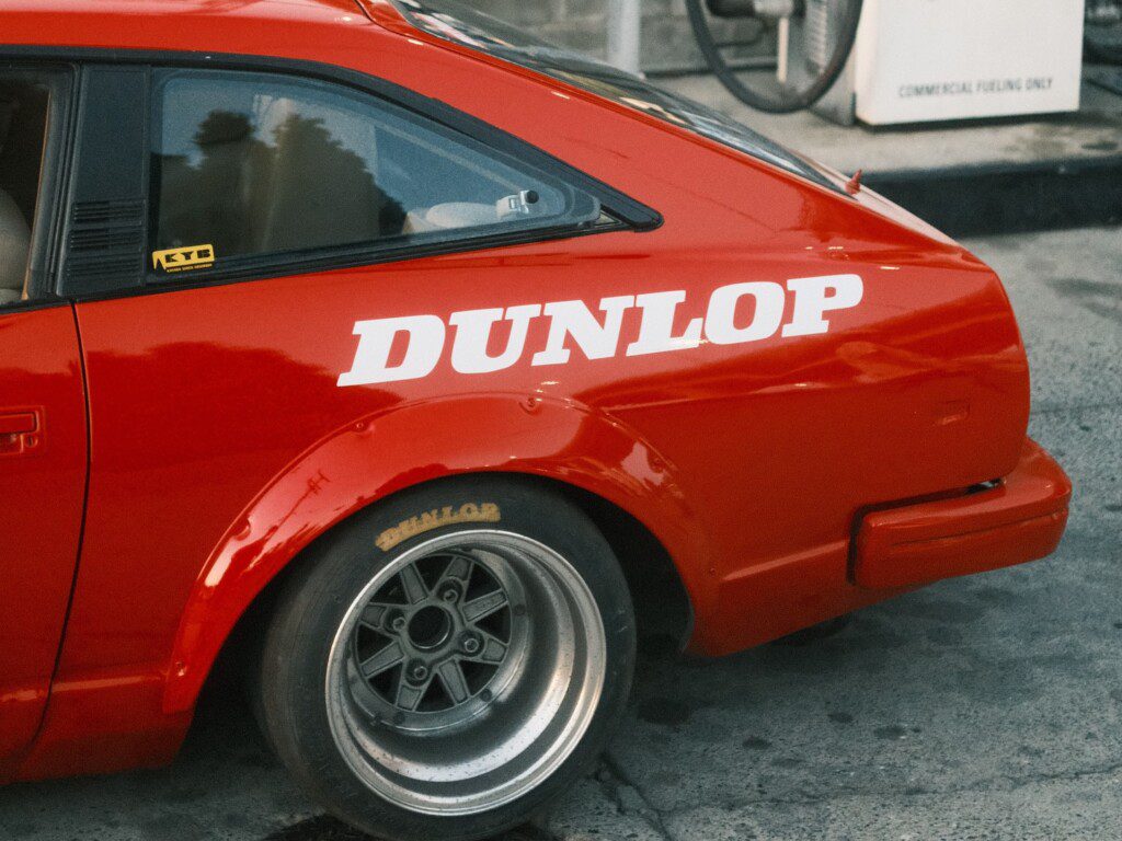 Red sports car with Dunlop branding and custom wheels at gas station.
