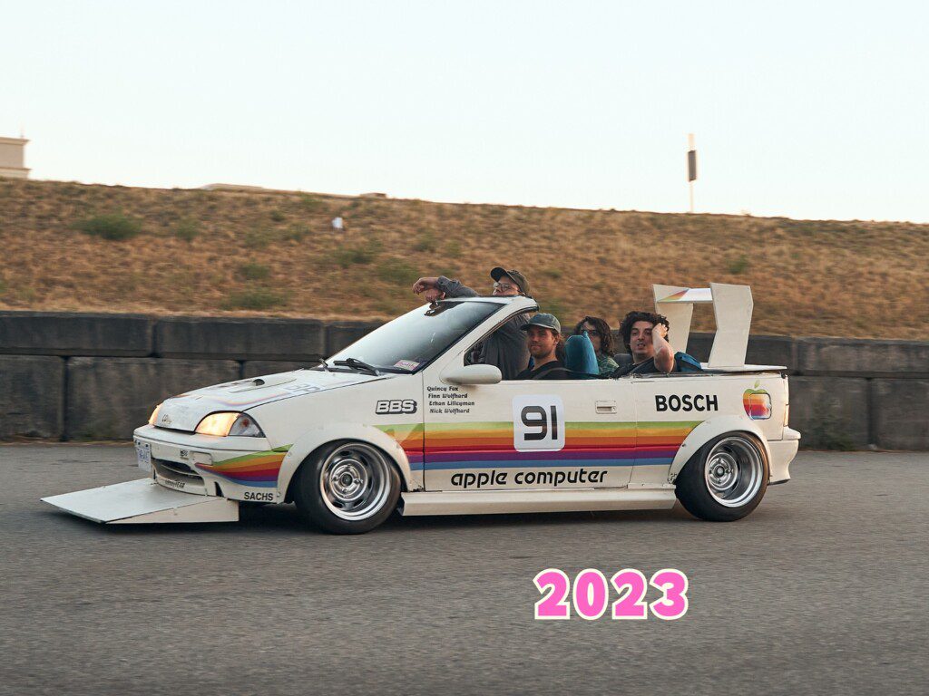 Retro-themed customized car with Apple branding and passengers, racing on track, 2023. Vintage style automotive design.