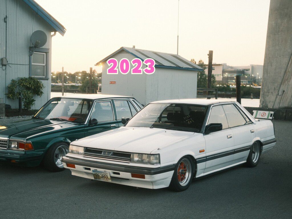 Vintage cars parked near water, showcasing retro automotive design with a 2023 text overlay.