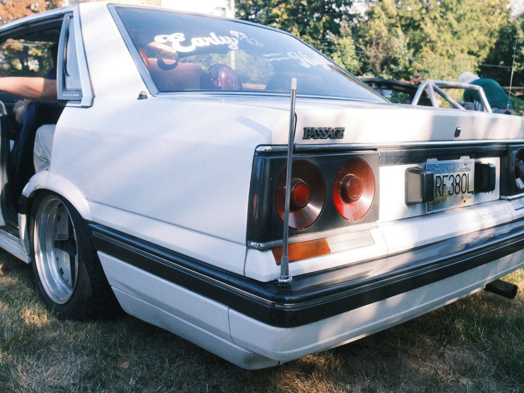 Vintage white car with Skyline badge parked on grass, featuring classic taillights and sleek rear design.
