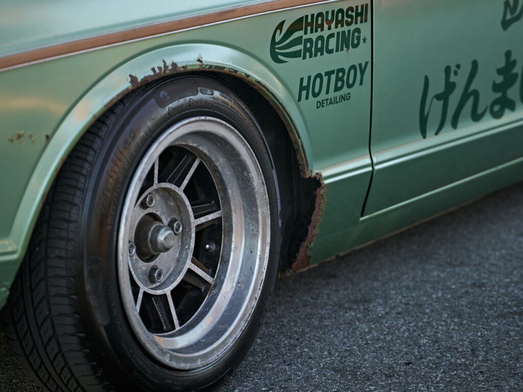 Close-up of a vintage car wheel with rusted fender and racing decals on the body.