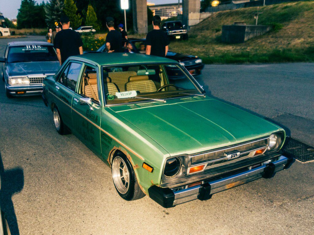 Vintage green car parked on a street with people in the background at sunset.