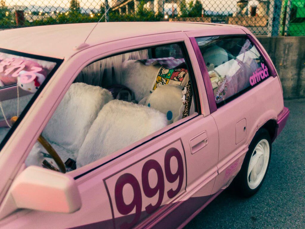 Pink car with plush interior and number 999 decal, parked by a fence. Playful and unique vehicle design.