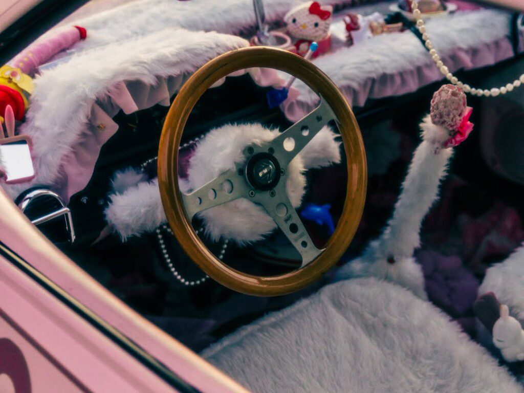 Cute car interior with fluffy decorations and steering wheel, featuring plush toys and pink accents for a personalized touch.
