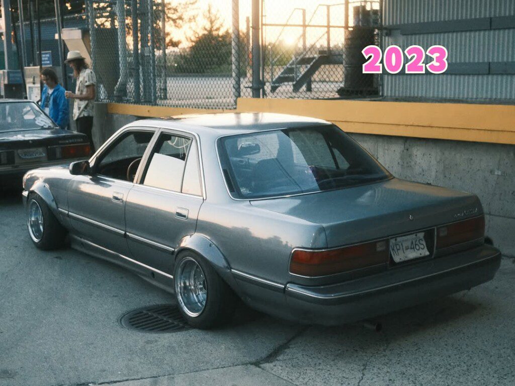 Vintage silver car at sunset in urban setting with 2023 text overlay. Retro automotive vibe.