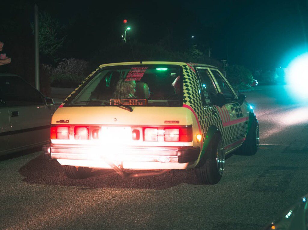 Vintage car with checkered design and glowing lights parked on a dimly lit street at night.