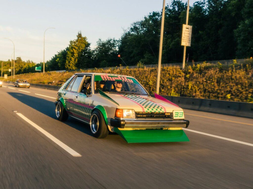 Vintage customized car with colorful paint job driving down a highway during golden hour.