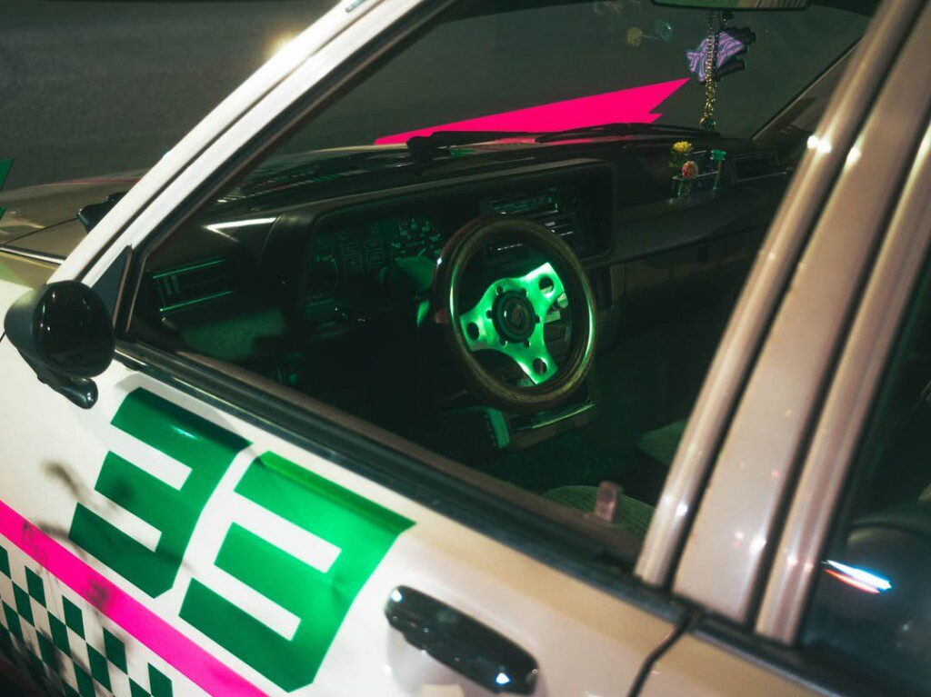 Close-up view of vintage car interior with neon lighting, featuring steering wheel and dashboard details.