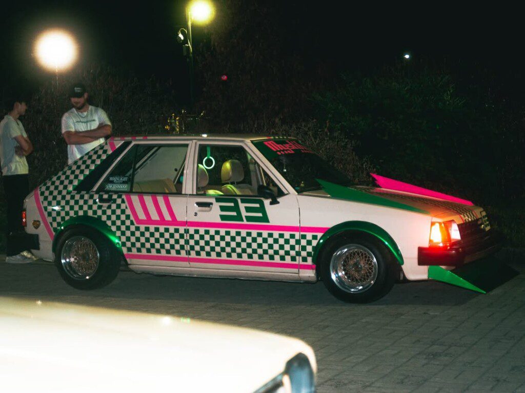 Retro car with green and pink checkered design at night, parked under streetlights.