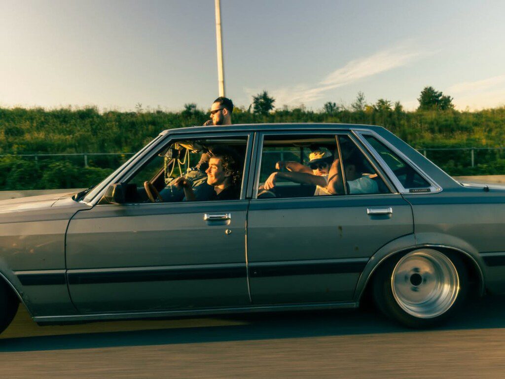 Vintage car cruising with friends on open road during sunset, showcasing classic style and freedom.