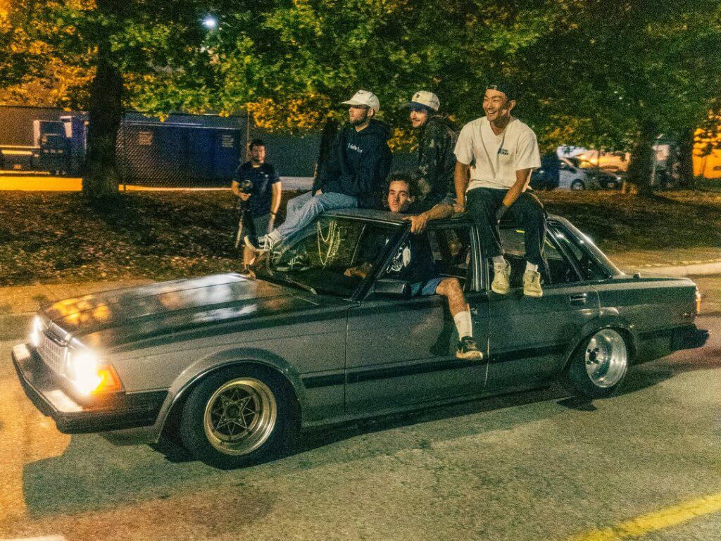 Group of friends enjoying a night ride on an old car, sitting casually while parked under city lights.