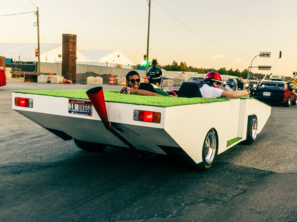 Unique custom car with turf surface drives on city street, driver and passenger enjoy the ride.