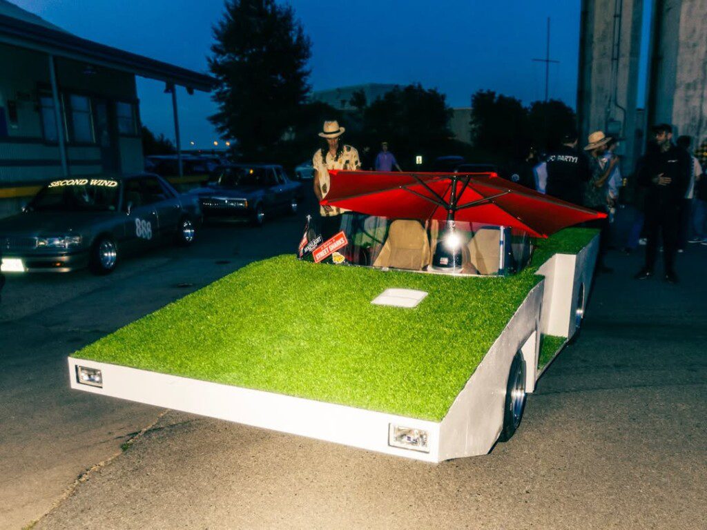 Creative car with grass exterior and red umbrella roof at night event. Unique automotive design.