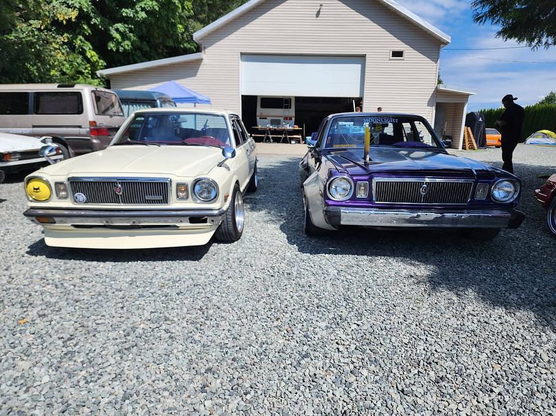 Two classic vintage cars parked on a gravel driveway in front of a garage.