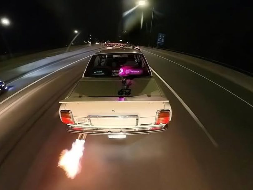 Vintage car with rear flame exhaust driving on highway at night.