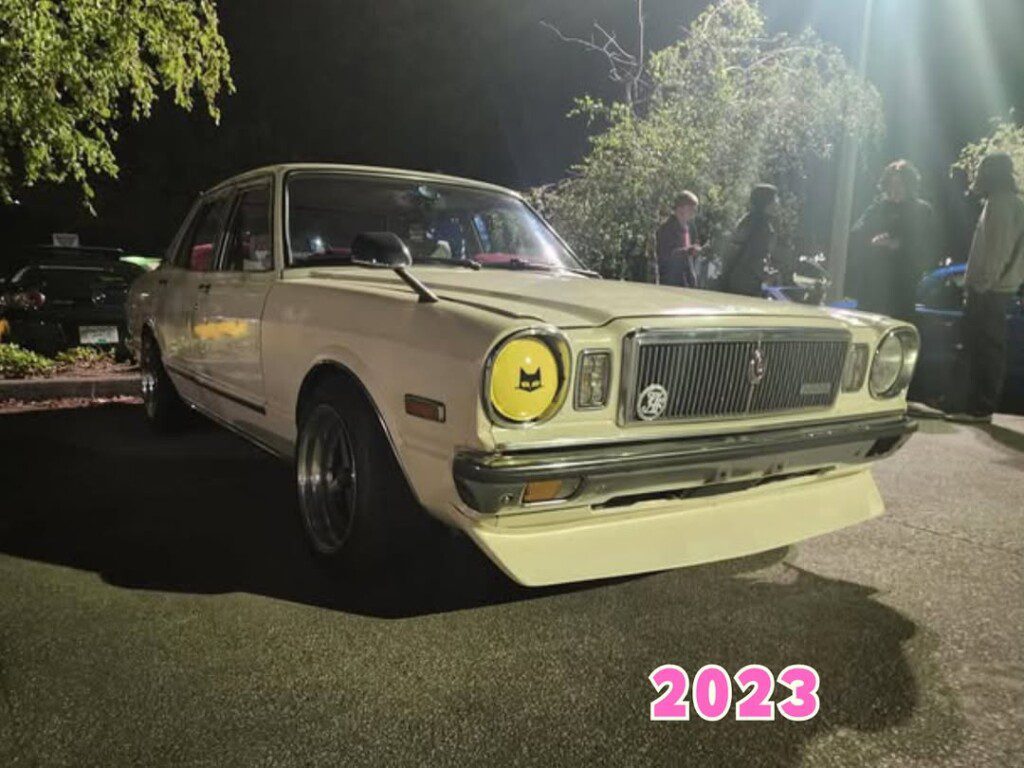 Classic car at a nighttime gathering, featuring customized yellow headlight and vintage grille, 2023.