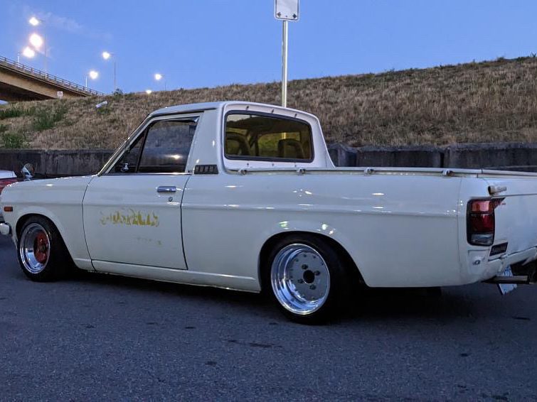 Vintage white pickup truck parked on street at dusk, with custom wheels and scenic backdrop.