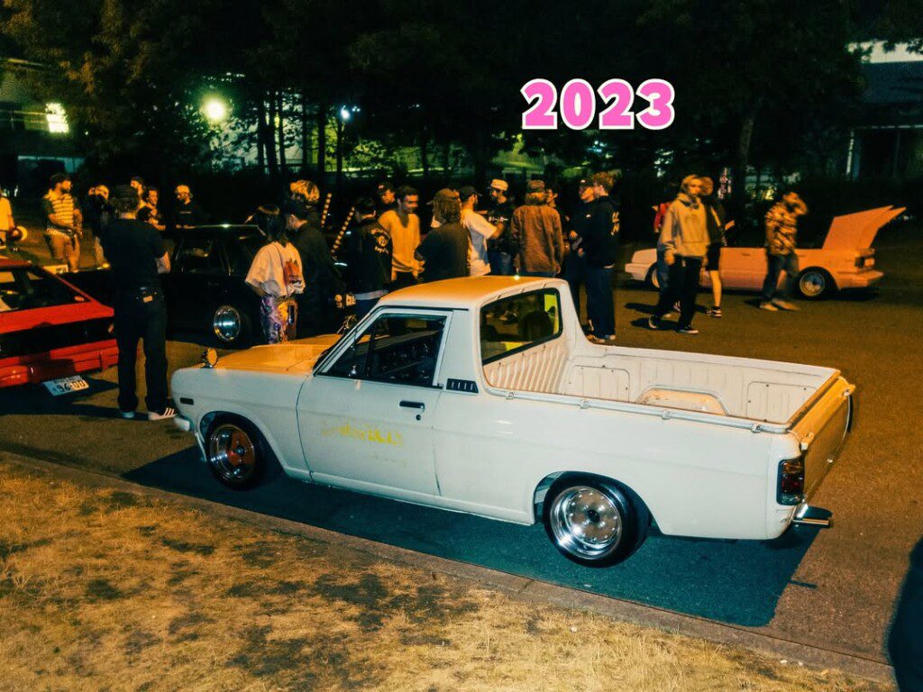 Night car meet in 2023 featuring vintage pickup and enthusiasts gathered around classic vehicles.