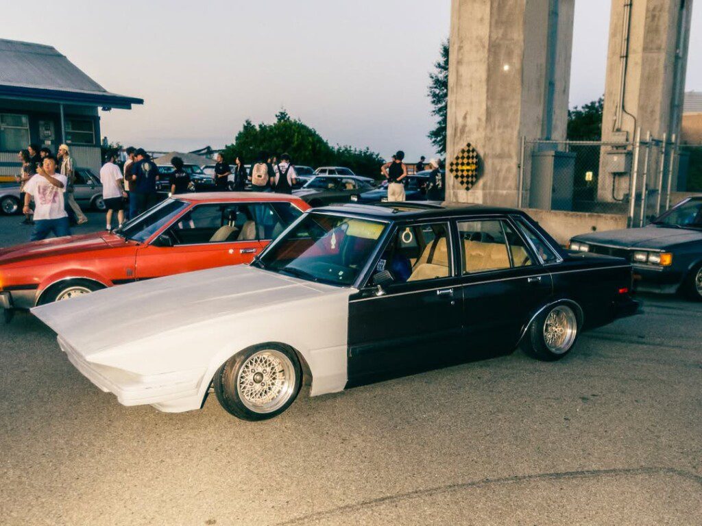 Modified classic car at a car meet with attendees in the background, showcasing custom design and detailing.