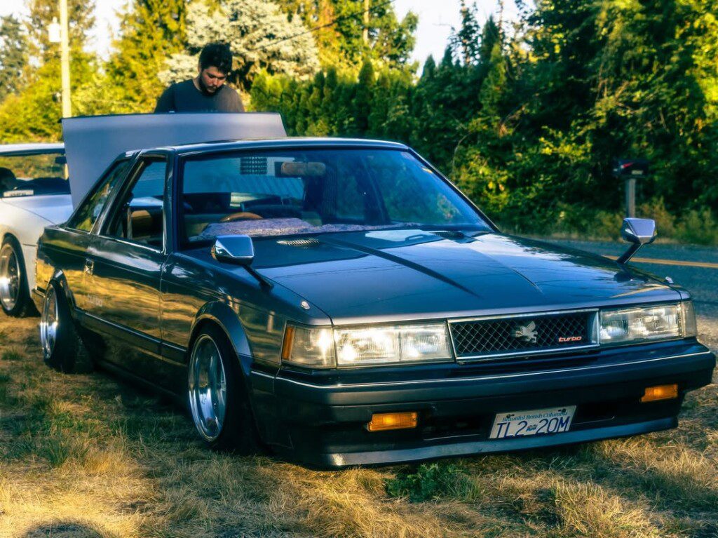 Vintage car with pop-up headlights and retro design, parked with open hood in a scenic outdoor setting.