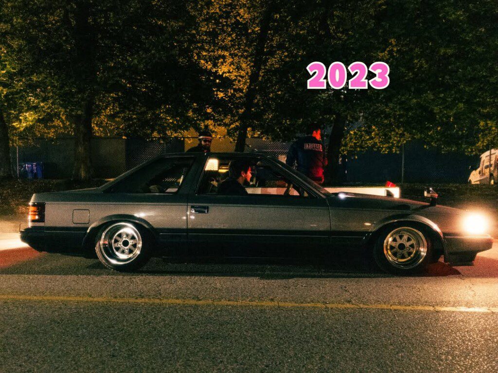 Classic car at night under streetlights with a 2023 overlay. Urban setting, highlighting vintage automotive style.